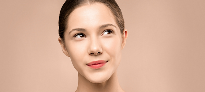 woman with glowing skin looking off to the side with a tan background