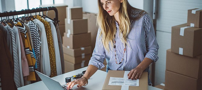 woman standing over a laptop with shipping boxes around her