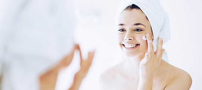 A young girl looks in the mirror as she applies a skin cleanser to her face